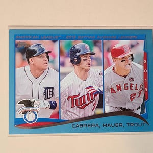 May include: A 2013 Topps American League Batting Average Leaders baseball card featuring Miguel Cabrera, Joe Mauer, and Mike Trout. The card has a light blue border, three individual player portraits, and the text Cabrera, Mauer, Trout.