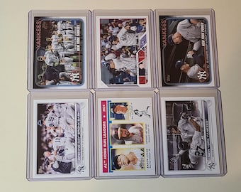 May include: Six baseball trading cards featuring New York Yankees players, encased in protective sleeves. The cards display action shots and team photos, with the Yankees logo and text visible. The cards are arranged in two rows of three.