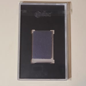 May include: A black plastic case with a clear plastic front, displaying a dark blue card with the word "PSA" in white lettering.