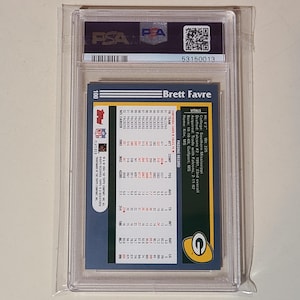 May include: A Brett Favre football card, encased in a protective plastic holder. The card's back features player statistics, team logos, and the text "Brett Favre". The card is graded and authenticated by PSA.
