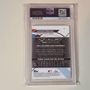 K&ouml;nnte beinhalten: Eine Baseballkarte in einer transparenten Kunststoffh&uuml;lle. Die Karte enth&auml;lt Informationen &uuml;ber Jordan Walker, einschlie&szlig;lich Gr&ouml;&szlig;e, Gewicht und Team. Die Karte tr&auml;gt die Aufschrift "Finest 2022 Minor League Performance" und ein PSA-Authentifizierungsetikett.