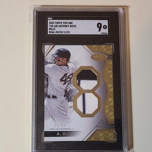 May include: A graded baseball card featuring Anthony Rizzo in a New York Yankees uniform. The card includes a dual patch relic and the text "2023 Topps Tier One". The card is graded a 9 and is numbered 11/25.