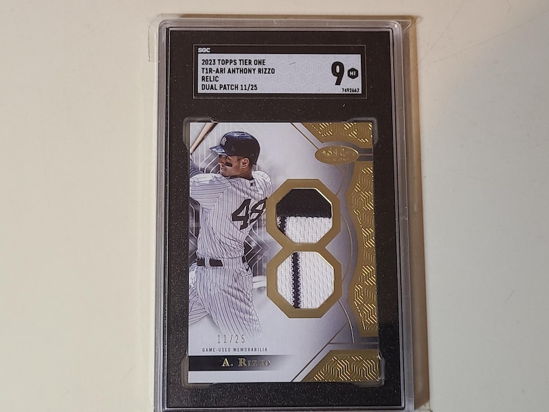 May include: A graded baseball card featuring Anthony Rizzo in a New York Yankees uniform. The card includes a dual patch relic and the text "2023 Topps Tier One". The card is graded a 9 and is numbered 11/25.
