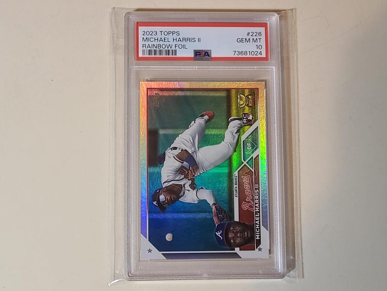 May include: A baseball card featuring Michael Harris II of the Atlanta Braves in a rainbow foil design. The card is graded GEM MT 10 and encased in a protective holder. The card's text includes "2023 Topps" and "Rainbow Foil".