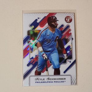 May include: A rectangular sports trading card featuring Kyle Schwarber of the Philadelphia Phillies. The player wears a light blue uniform with the number 12, a helmet, and batting gloves while holding a bat. The background has a white, red, and blue graphic pattern with a holographic finish.