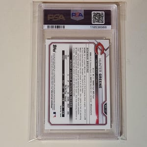 May include: A PSA-graded Hunter Greene baseball card encased in a clear plastic holder. The back of the card features the Cincinnati Reds logo, player statistics, and a Bowman Briefing section detailing pitching records and career highlights.