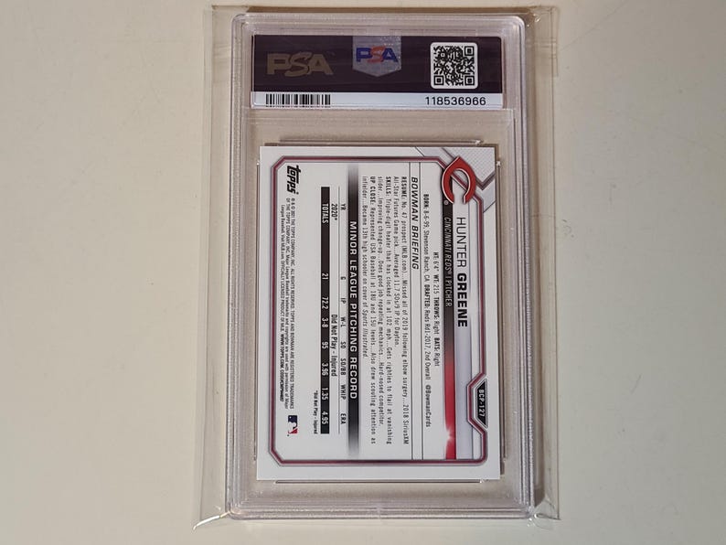 May include: A PSA-graded Hunter Greene baseball card encased in a clear plastic holder. The back of the card features the Cincinnati Reds logo, player statistics, and a Bowman Briefing section detailing pitching records and career highlights.