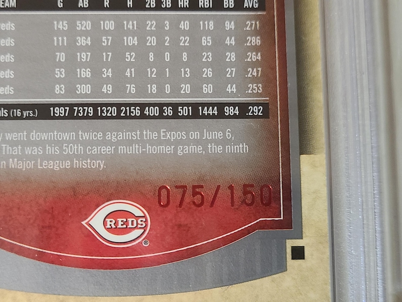 May include: A baseball card featuring the Cincinnati Reds logo and team information. The card has a red and white design with the team's logo prominently displayed. The card is numbered 075/150.