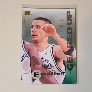 May include: A basketball trading card featuring a player in a white and purple jersey. The card has the text "GEARED UP" and "KIDD" on the side. The card also has the word "Emotion" and a holographic "E" on the front.