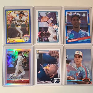 May include: Six baseball trading cards featuring Moises Alou in various team uniforms. The cards are encased in protective sleeves. The cards showcase action shots and portraits, with team logos and player names prominently displayed.
