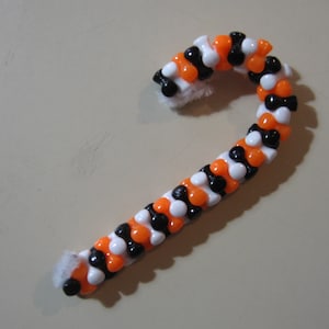 May include: A candy cane-shaped beaded bracelet with alternating black, white, and orange beads.