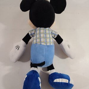 May include: A plush Mickey Mouse toy wearing a blue and yellow plaid shirt, blue jeans, and blue shoes.
