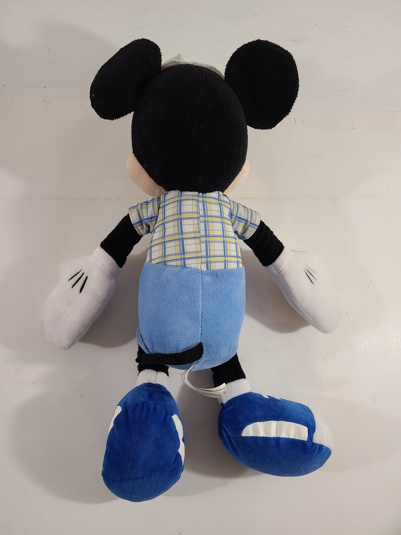 May include: A plush Mickey Mouse toy wearing a blue and yellow plaid shirt, blue jeans, and blue shoes.
