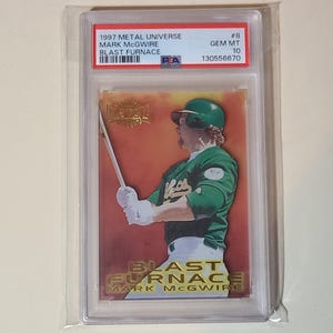 May include: A baseball card featuring Mark McGwire in a green and white uniform, holding a bat. The card is from the 1997 Metal Universe series, titled "Blast Furnace." The card is encased in a protective holder with text that reads "GEM MT 10."