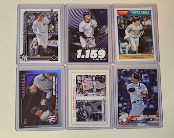 May include: Six individual baseball trading cards featuring Aaron Judge in a New York Yankees uniform. Each card is encased in a clear protective plastic sleeve. The cards display various action shots, team logos, and text including OPS LEADER 1.159.