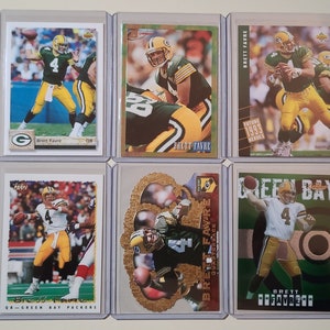 May include: Six different trading cards featuring Brett Favre, a former American football quarterback. The cards are all in protective plastic sleeves and feature different photos of Favre in his Green Bay Packers uniform. The cards are from different years and have different designs.