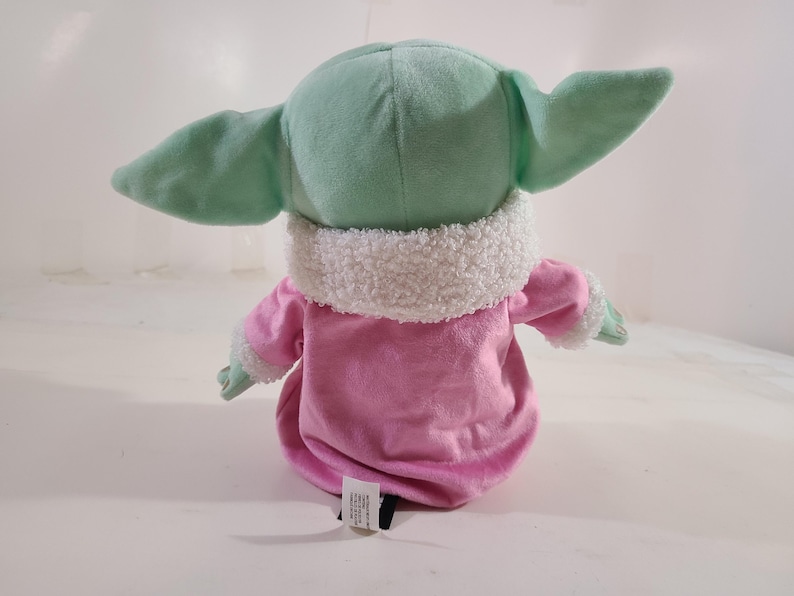 Pu&ograve; includere: Un peluche di un personaggio con grandi orecchie e un abito rosa. Il giocattolo ha una testa e orecchie verde menta, un indumento rosa simile a una veste e un colletto bianco e soffice. Il giocattolo &egrave; progettato per assomigliare a un personaggio popolare.