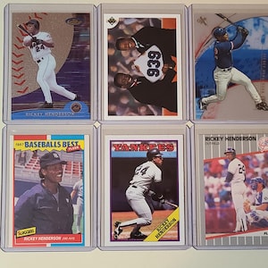 May include: Six baseball trading cards featuring Rickey Henderson in various poses. The cards are encased in protective sleeves. The cards display the player in action, with team logos and player information. The cards are from different sets and eras.