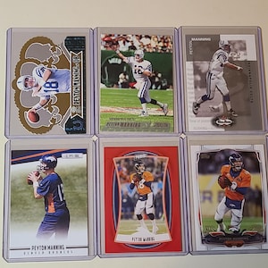 May include: Six Peyton Manning football trading cards in protective sleeves. The cards feature images of Manning in various uniforms, including the Indianapolis Colts and Denver Broncos. The cards are in various designs and styles.