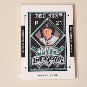 May include: A baseball card featuring Roger Clemens, a former pitcher for the Boston Red Sox. The card includes a patch with the text "RED SOX" and "MVP CLEMENS". The card is from the "UD Patch Collection" and commemorates the 1986 American League MVP.