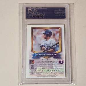 May include: A professionally graded Roberto Alomar baseball card encased in a clear plastic PSA holder. The card features a photograph of the player in a Blue Jays uniform, with text detailing his stats, position as 2B, and his 1992 ALCS MVP award.