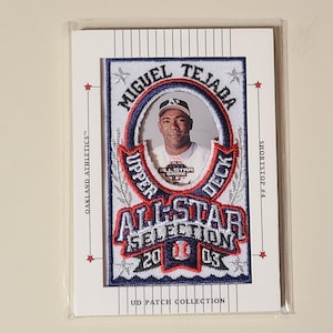 May include: A baseball trading card featuring Miguel Tejada, an Oakland Athletics player. The card has a patch with the words "All-Star Selection 2003" and "Upper Deck." The card is in a protective sleeve.