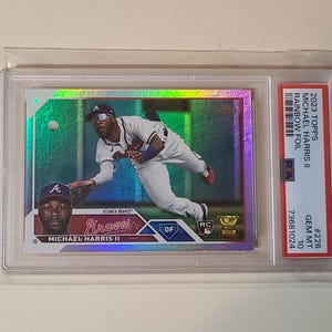May include: A baseball trading card featuring Michael Harris II of the Atlanta Braves in a rainbow foil design. The card is graded GEM MT 10 and encased in a protective holder. The card's text includes "2023 Topps" and "Rainbow Foil".
