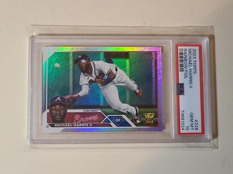 May include: A baseball trading card featuring Michael Harris II of the Atlanta Braves in a rainbow foil design. The card is graded GEM MT 10 and encased in a protective holder. The card's text includes "2023 Topps" and "Rainbow Foil".
