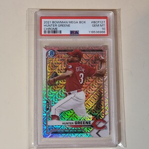 May include: A 2021 Bowman Mega Box Hunter Greene Chrome baseball card, graded PSA Gem Mt 10, #BCP127. The card features a holographic, geometric pattern background with the pitcher in a red jersey and white pants, encased in a clear plastic slab.