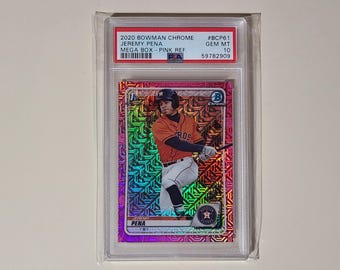 May include: A baseball card featuring Jeremy Pena in an orange and white uniform, with the text "HOUSTON" on the front. The card is encased in a protective holder. The card has a pink and iridescent background with the text "2020 Bowman Chrome" and "Mega Box - Pink Ref."