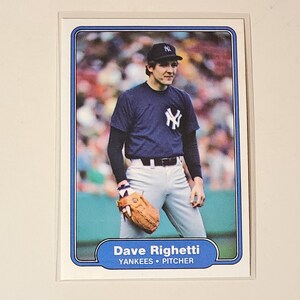 May include: Baseball card featuring Dave Righetti of the New York Yankees. The card shows Righetti in a navy blue uniform with the Yankees logo, a black cap, and a brown baseball glove. The card has a blue border and the player's name and position are printed at the bottom.