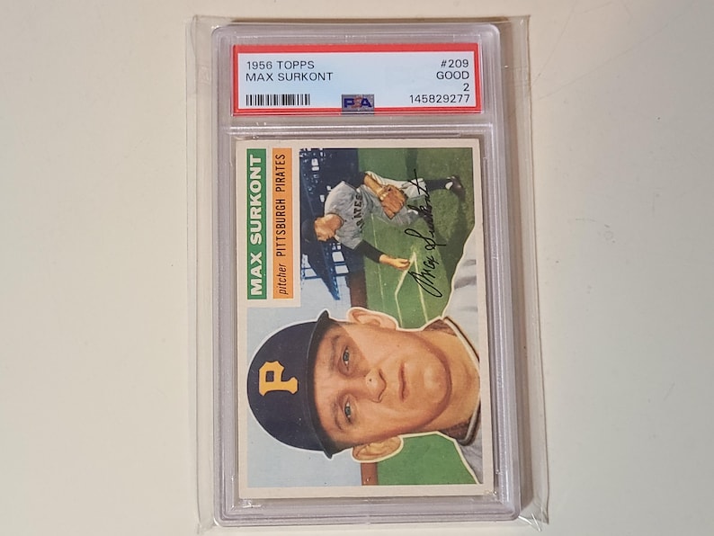 Pu&ograve; includere: Una figurina da baseball Topps del 1956 di Max Surkont, classificata GOOD 2 da PSA, in una custodia di plastica trasparente. La carta presenta un ritratto del lanciatore dei Pittsburgh Pirates con un berretto nero con una P gialla.