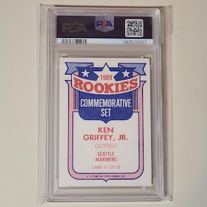 Peut inclure: Une carte de baseball 1989 Topps Rookies Commemorative Set repr&eacute;sentant Ken Griffey, Jr. des Seattle Mariners, identifi&eacute;e comme la carte 11 sur 33. La carte est scell&eacute;e dans un &eacute;tui de protection rigide PSA avec une &eacute;tiquette noire et un QR code.