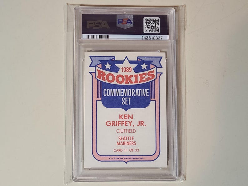 Peut inclure: Une carte de baseball 1989 Topps Rookies Commemorative Set repr&eacute;sentant Ken Griffey, Jr. des Seattle Mariners, identifi&eacute;e comme la carte 11 sur 33. La carte est scell&eacute;e dans un &eacute;tui de protection rigide PSA avec une &eacute;tiquette noire et un QR code.