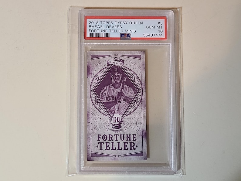 May include: A baseball card encased in a protective holder. The card features Rafael Devers from the 2018 Topps Gypsy Queen series, labeled as a "Fortune Teller Minis" card. The card is graded as GEM MT 10.