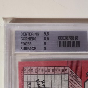 Peut inclure: Une carte de baseball class&eacute;e et encadr&eacute;e dans un support en plastique transparent. L'&eacute;tiquette argent&eacute;e affiche les d&eacute;tails de la classification : scores de centrage, de coins, de bords et de surface. Un code-barres et un num&eacute;ro de s&eacute;rie sont &eacute;galement pr&eacute;sents.