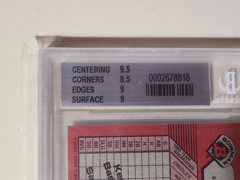 Peut inclure: Une carte de baseball class&eacute;e et encadr&eacute;e dans un support en plastique transparent. L'&eacute;tiquette argent&eacute;e affiche les d&eacute;tails de la classification : scores de centrage, de coins, de bords et de surface. Un code-barres et un num&eacute;ro de s&eacute;rie sont &eacute;galement pr&eacute;sents.