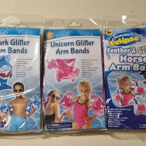 May include: Three packages of inflatable arm bands for kids. The arm bands are decorated with glitter and feature a shark, unicorn, and horse. The packages include safety information and size details.