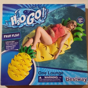 May include: A yellow pineapple-shaped inflatable pool float with a green top and a woman laying on it. The box reads "H₂O GO! Fruit Float" and "One Lounge". The box also has a warning that says "This is not a lifesaving device. Do not leave child unattended while device is in use." The box is blue and white with the Bestway logo.