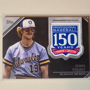 May include: A Topps baseball card featuring Robin Yount of the Milwaukee Brewers. The card includes a commemorative patch celebrating 150 years of professional baseball, with the years 1869-2019. The player is wearing a Brewers uniform.