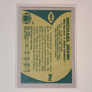 May include: A vintage Michael Irvin football card from the 1988 Topps series. The card features a green and tan design with player stats and biographical information. The card is in a protective sleeve.