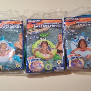 May include: Three inflatable pool rings for kids. The rings are shaped like a shark, alligator, and dolphin. Each ring has a colorful design and the words "Snack Attack" and "Adventure Swim Ring" printed on them.