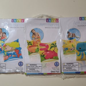 May include: Three packages of Intex arm bands for children. Each package features a different design: mermaid, dinosaur, and sea buddy. The arm bands are 7 inches by 7 inches and are for children ages 3-6. The packages have a warning label about choking hazards.