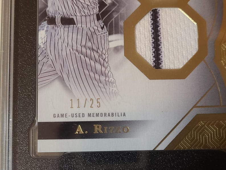 May include: A baseball card with a player in a pinstripe uniform. The card includes a fabric patch and the text "GAME-USED MEMORABILIA." The card is numbered 11/25 and has the player's name, A. Rizzo, at the bottom.