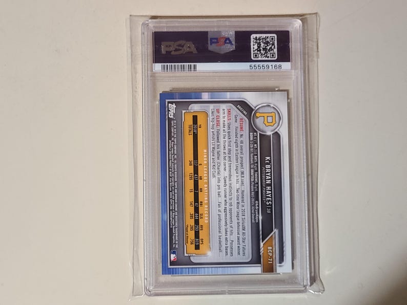 Puede incluir: Una tarjeta de b&eacute;isbol de Ke'Bryan Hayes, dentro de un soporte de pl&aacute;stico transparente. La tarjeta presenta el logotipo de los Piratas de Pittsburgh y la informaci&oacute;n del jugador. La tarjeta est&aacute; calificada por PSA, con un n&uacute;mero de serie visible.