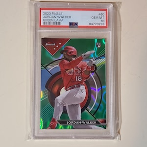K&ouml;nnte beinhalten: Eine Baseball-Sammelkarte von Jordan Walker in einer Schutzh&uuml;lle. Die Karte zeigt einen Spieler in roter Uniform mit der Nummer 18, vor einem gr&uuml;nen und roten Hintergrund. Die Karte ist mit "2023 Finest" und "Green Lava" beschriftet.