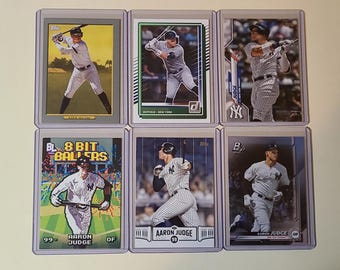 May include: Six baseball trading cards featuring Aaron Judge of the New York Yankees. The cards are in protective cases. The cards show Judge in various action poses, including batting and running. Some cards have the text "8 BIT BALLERS" and "AARON JUDGE".