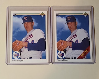 May include: Two baseball cards featuring Nolan Ryan in a Texas Rangers uniform. The cards are in protective cases. The cards show Ryan wearing a blue cap with a white and red "T" logo and holding a baseball glove. One card has "300th Win!" text.