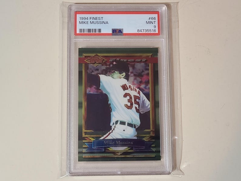Puede incluir: Una tarjeta de b&eacute;isbol Mike Mussina de 1994 Topps Finest, calificada como Mint 9 por PSA. La tarjeta muestra a un jugador con uniforme blanco y el n&uacute;mero 35 en la espalda, encapsulada en un estuche de pl&aacute;stico transparente con etiqueta blanca.