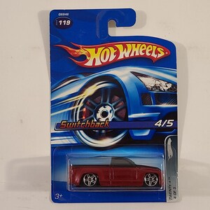 May include: A red Hot Wheels Switchback toy car on a blue and silver card with the words "Hot Wheels" and "Switchback" printed on it. The car is a pickup truck with black wheels and a black interior. The card also has the number "4/5" printed on it.